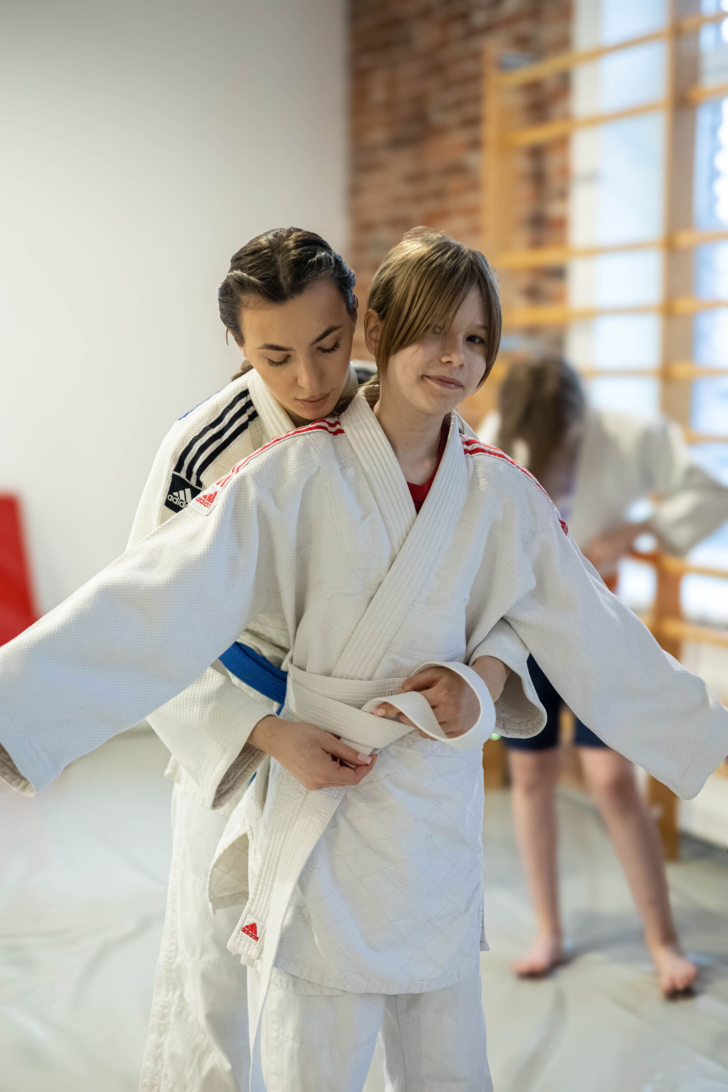 Trenerka Kame Gym pomaga zawiązać pas na treningu judo